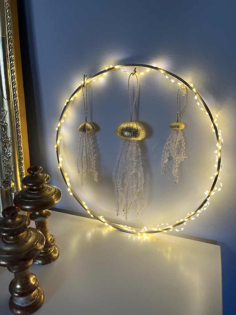 Composition formée de trois suspensions en forme de méduses "Néréis" réalisées à partir d'un oursin doré à la feuille d'or 22 carats et parées de filaments dorés et de tentacules en tulle blanc plissé et brodé de fils dorés: moyenne méduse à l'oursin bicolore à gauche, grande méduse au centre et petite méduse à droite